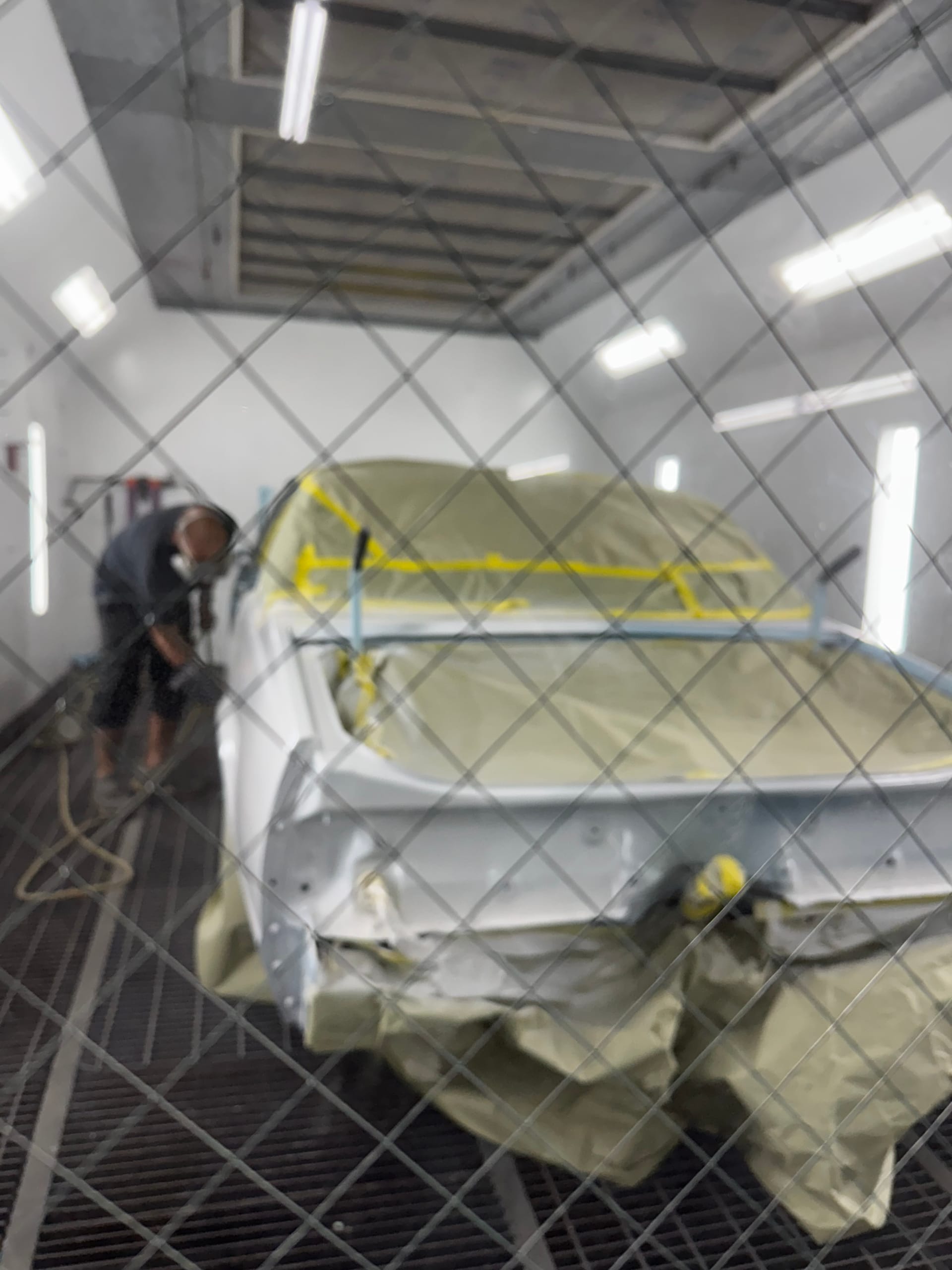Silver sedan masked in the paint booth, rear view, quarter panels in primer