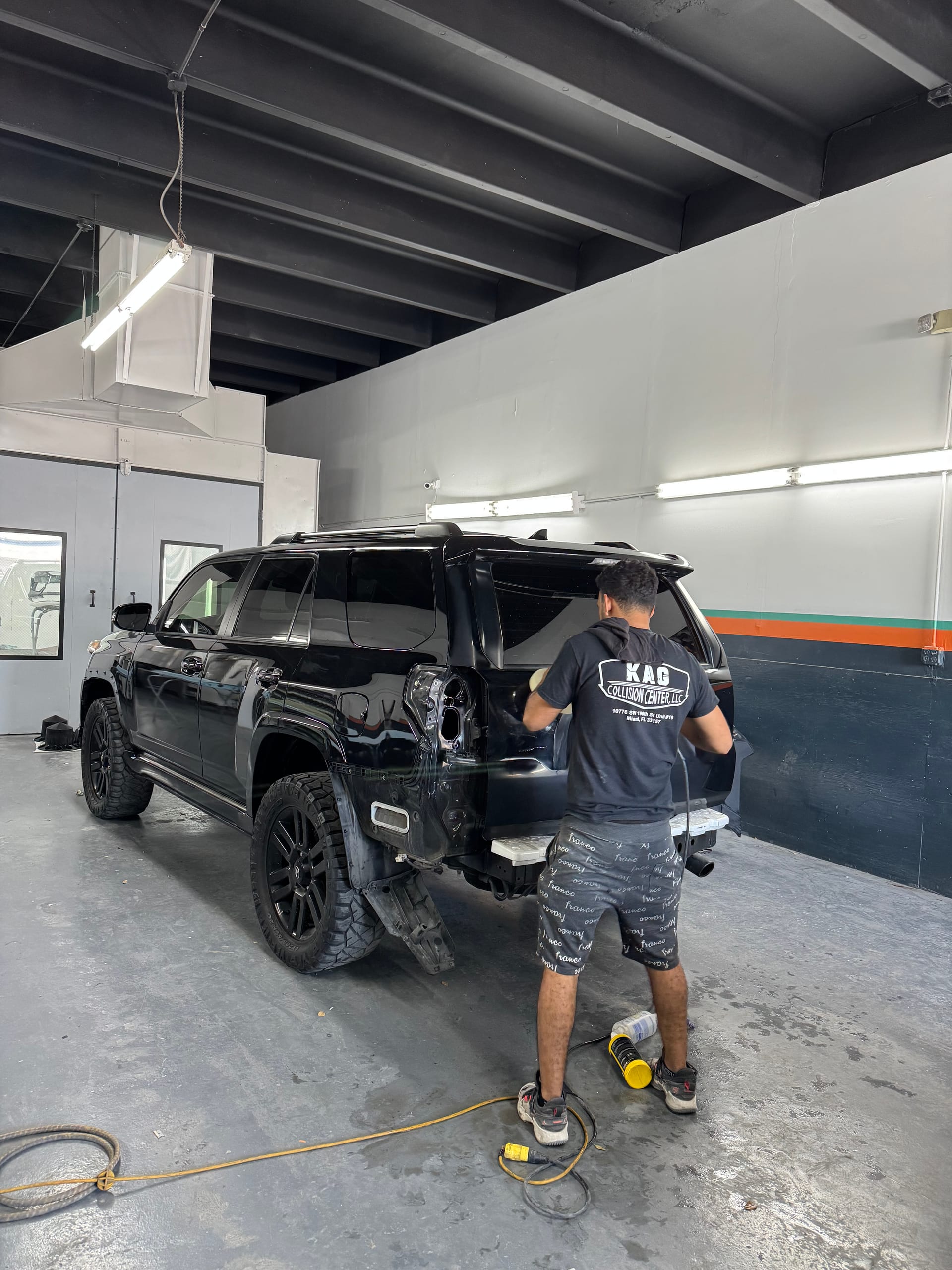Technician sanding the rear quarter of a black Toyota 4Runner on the shop floor