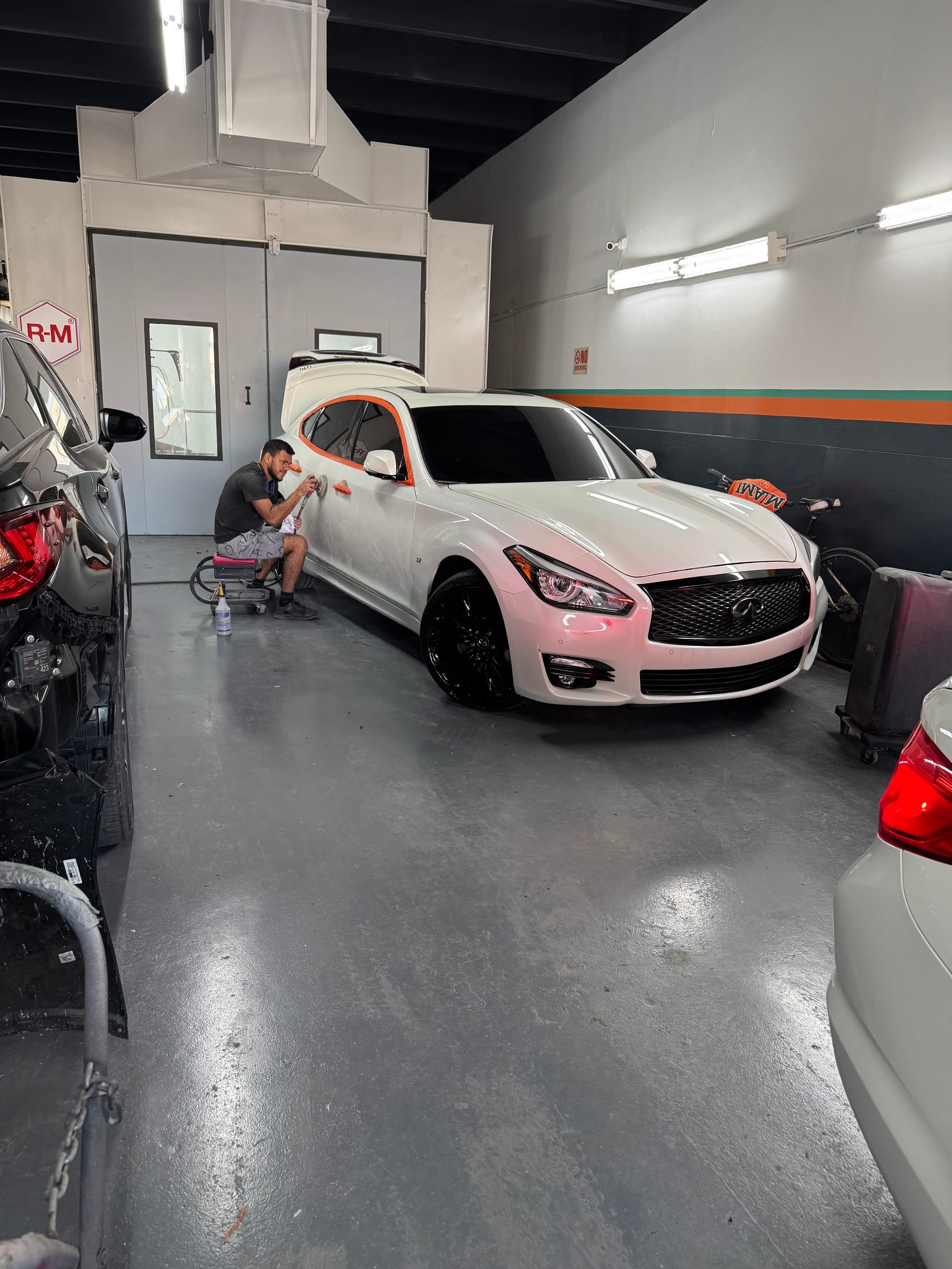 KAG technician sanding a white Infiniti sedan before paint